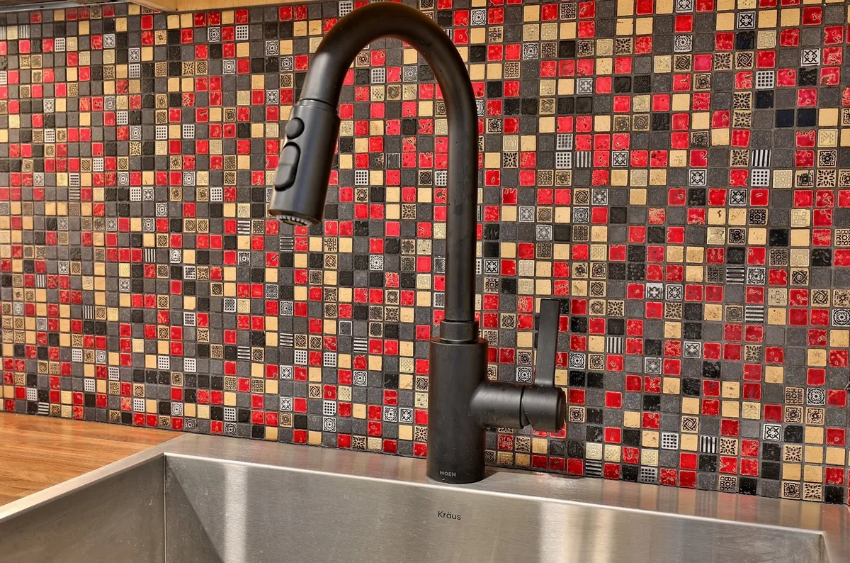 A modern kitchenette featuring a black faucet, vibrant mosaic backsplash, and a stainless steel sink. The countertop space is functional and welcoming, ideal for preparing quick meals or snacks. The overall ambiance is lively and family-friendly, with a setup conducive to casual gatherings.