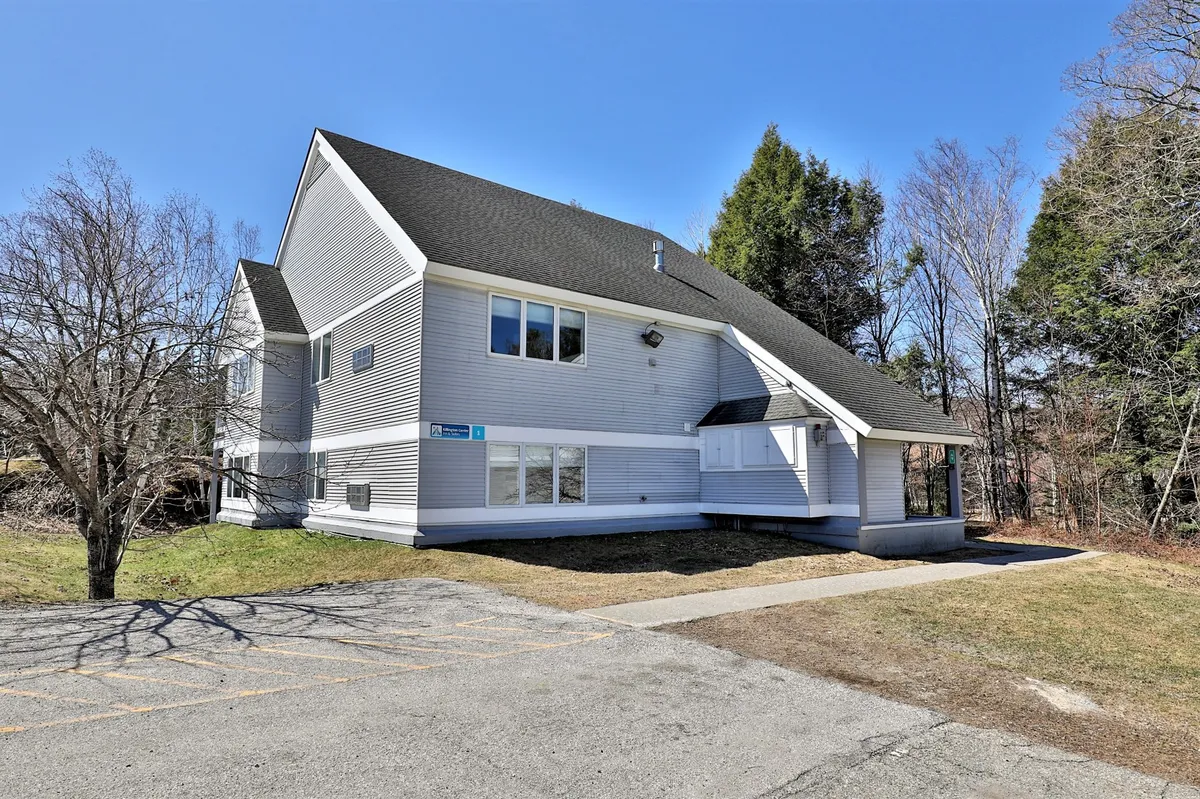 This exterior image showcases the building's modern architecture with expansive windows that overlook the surrounding natural landscape. The gentle curves of the structure and the visible trees evoke a sense of connection to the outdoors, hinting at nearby mountain activities and the welcoming environment awaiting guests.