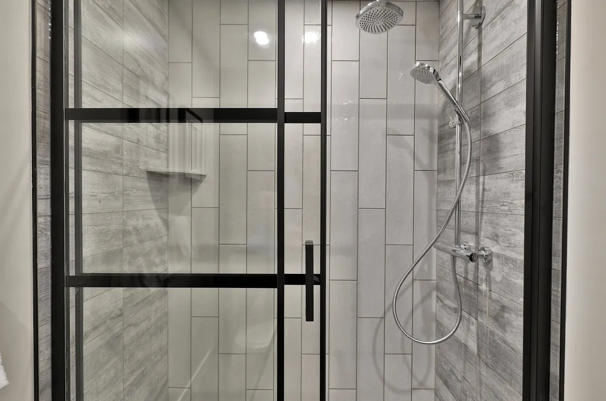 A stylish modern bathroom with a glass shower enclosure, contemporary fixtures, and textured tiles. The room is bright and clean, radiating a spa-like ambiance. The shower area looks inviting and has a high-end, rejuvenating atmosphere.